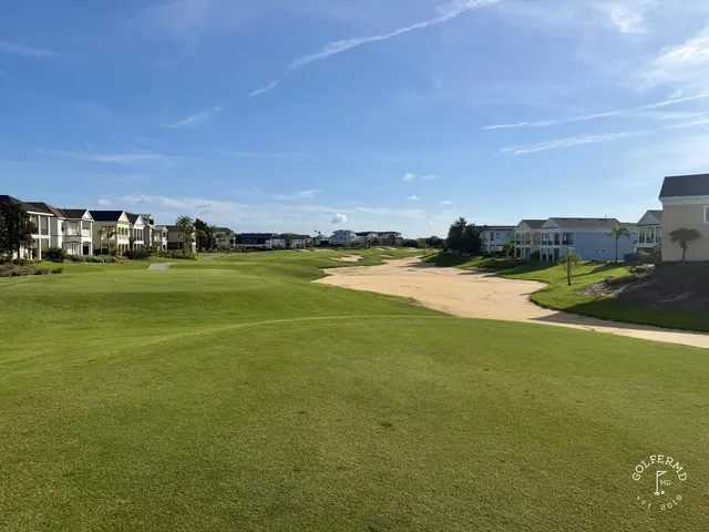 A wide view of the Palmer Course, with a pond, pine trees, and a sand bunker in the foreground.