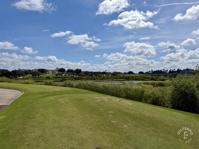 A green and flagstick at the Palmer Course, with a pond and fountain behind the green and palm trees along the water.