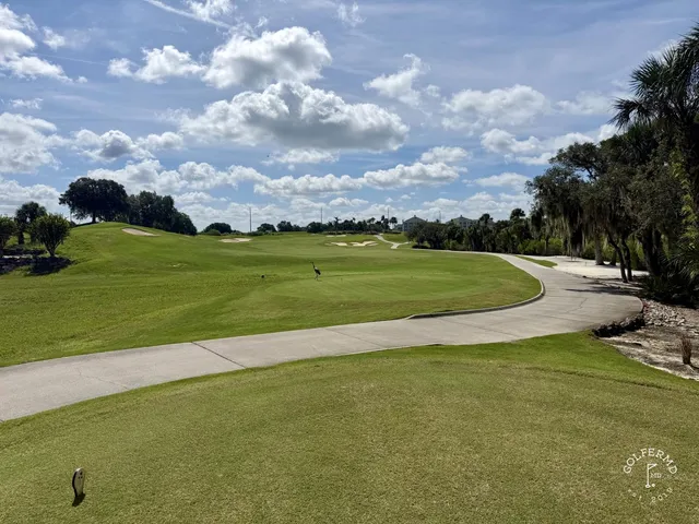 A green and flagstick at the Palmer Course, with a sand bunker in front and pine trees around the hole.