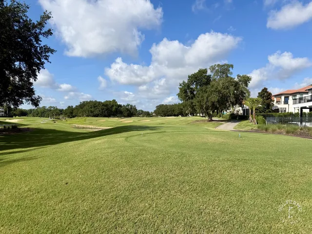 A green and flagstick at the Watson Course, with a pond in front and palm trees along the water.