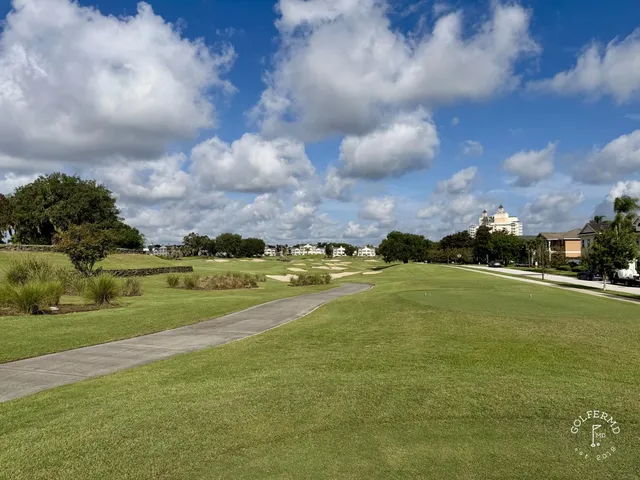 A fairway at the Watson Course lined with pine and palm trees, with a pond along the right side.