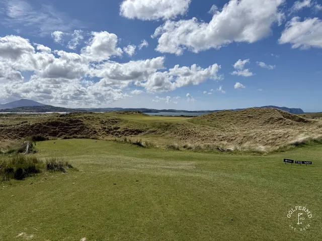 A golfer hitting a shot on the Sandy Hills, with the fairway and the water ahead.