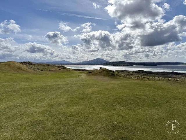 A golfer putting on a green on the Sandy Hills, with the water beyond the hole.