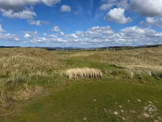 A close view of a flagstick on the Sandy Hills, with the bay behind the green.