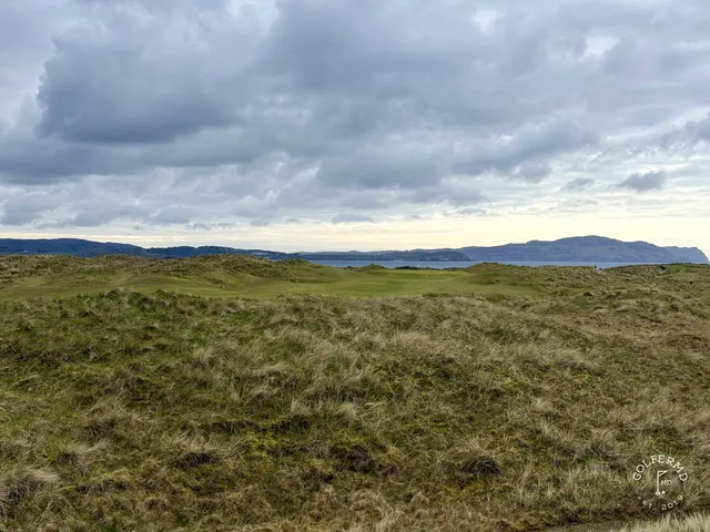 A group of golfers on the Sandy Hills, with the water behind them.