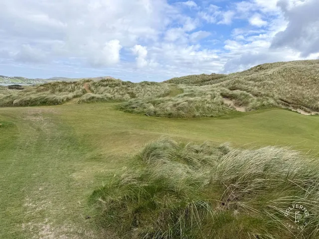 A green and flagstick on St. Patrick's, with a bunker in front and the ocean behind the hole.