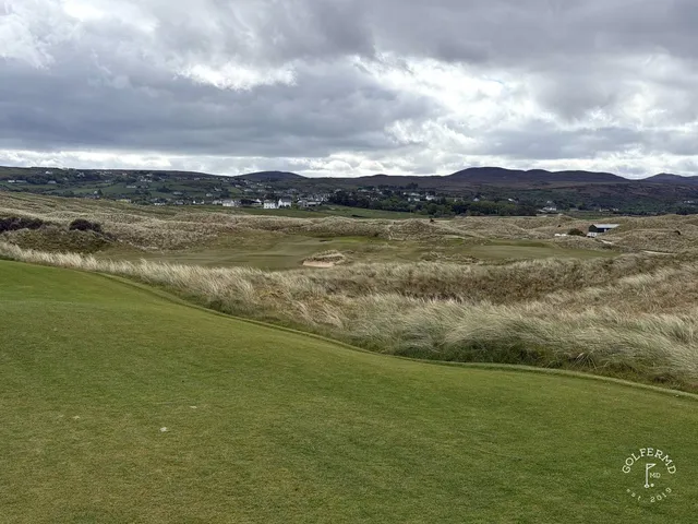 A close view of a green and flagstick on St. Patrick's, with the water behind it.