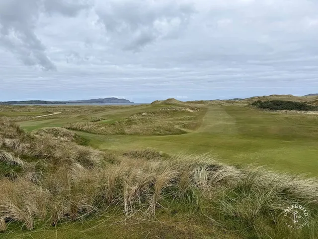A fairway and green on St. Patrick's, with a bunker in the foreground and the bay beyond.
