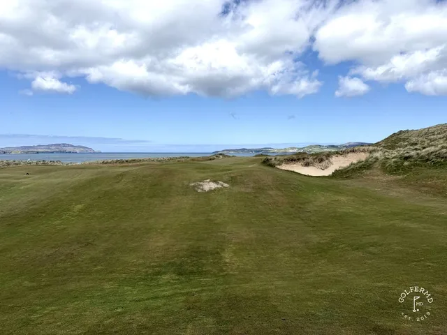 A golfer hitting a shot from the dunes on St. Patrick's, with the ocean ahead.