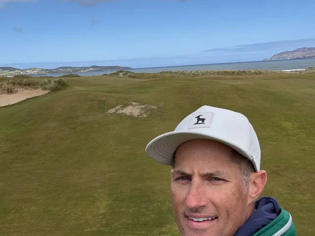A green and flagstick on St. Patrick's, with sand in front and the mountains beyond.