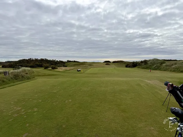 A green and flagstick on the Annesley Links above the dunes, with the mountains filling the background.