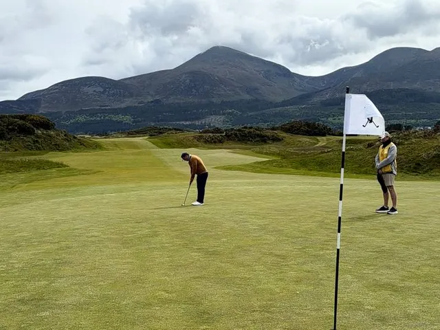 A green at Royal County Down with the flagstick, sand around the hole, and the Mournes beyond.