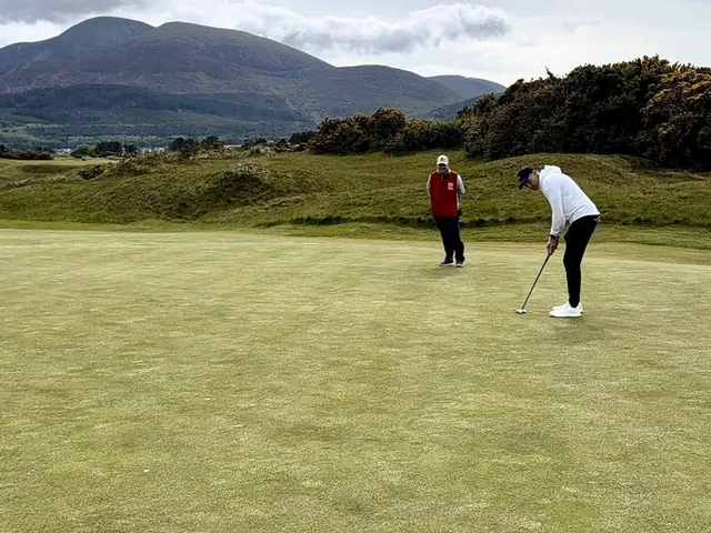 A golfer hitting an approach at Royal County Down, with the bay behind the green.