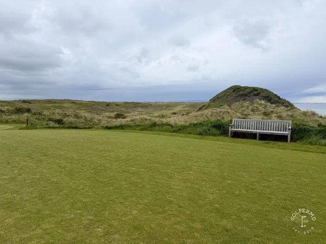 A fairway at Royal Portrush bending through the dunes toward a distant green.
