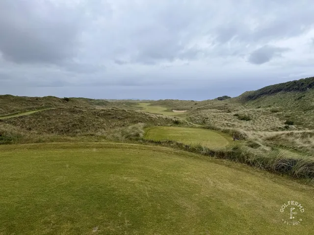 A green and flagstick at Royal Portrush seen from the fairway, with the sea on the horizon.