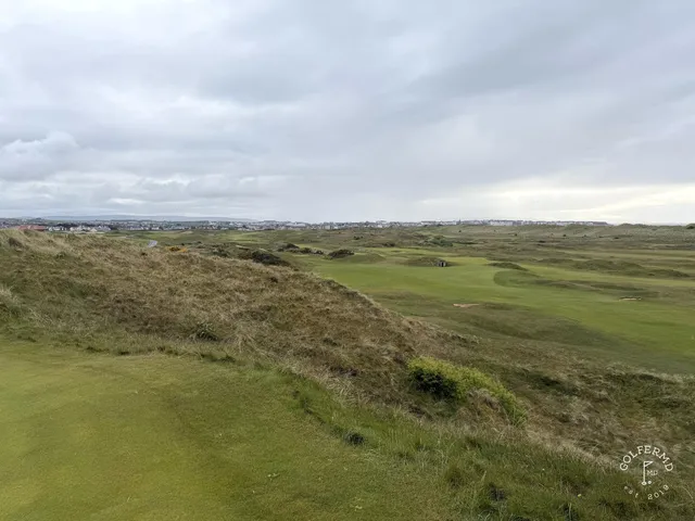 A green at Royal Portrush with the flagstick, sand around the hole, and the sea beyond.