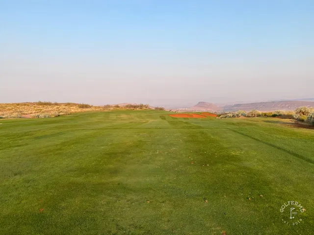 A green at Sand Hollow with the flagstick, sand around the hole and the cliffs beyond.