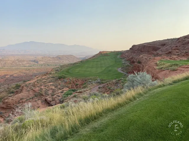 A wide view at Sand Hollow, the green in the foreground and the cliffs across the desert.