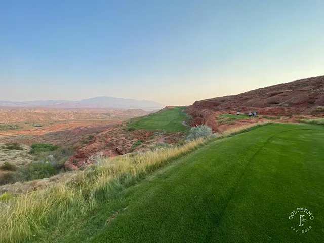 A green and flagstick at Sand Hollow, sand in front of the hole and the cliffs on the horizon.