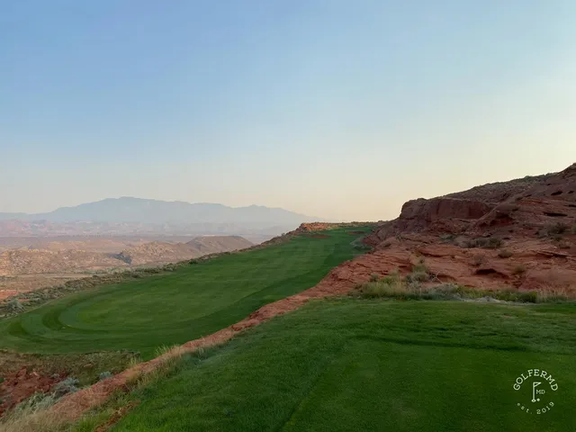 A green at Sand Hollow guarded by sand, with the red rock formations behind.