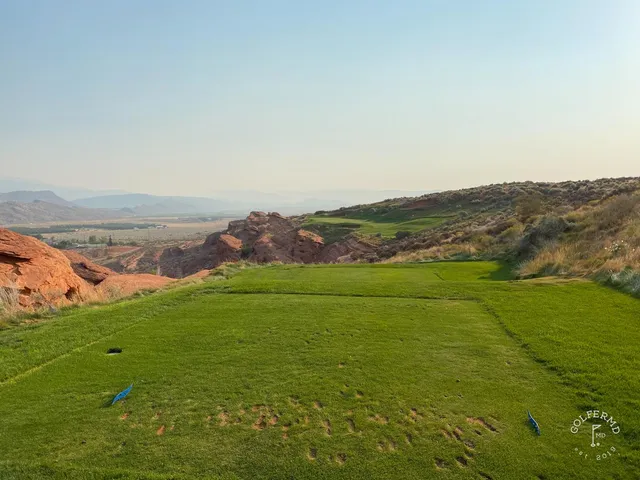 A green and flagstick at Sand Hollow seen from the fairway, with the red cliffs filling the background.
