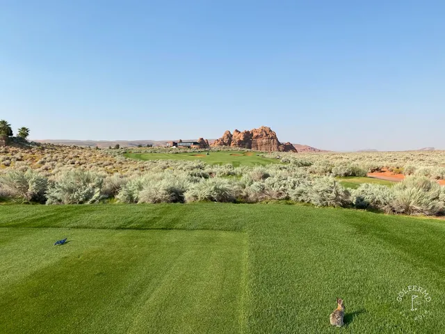 A fairway at Sand Hollow bending toward the cliffs, with a bunker on the right.