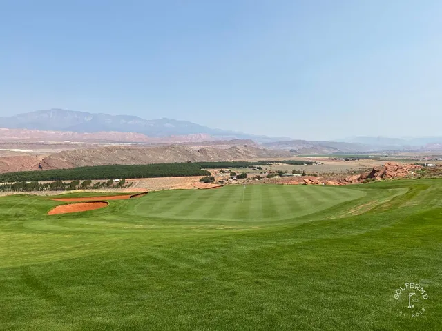 An elevated view across Sand Hollow, fairways and bunkers in front of the cliffs.