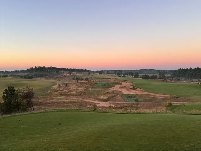 A wide view at Sand Valley, sandy ground stretching toward a distant green.