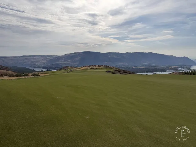 A tee at Scarecrow looking across sand toward a green and the mountains.