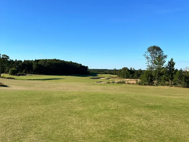 A green and flagstick at Sedge Valley, with a bunker in front and the sand hills beyond.