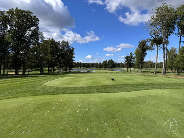 A green and flagstick at SentryWorld, a bunker in front and trees behind.