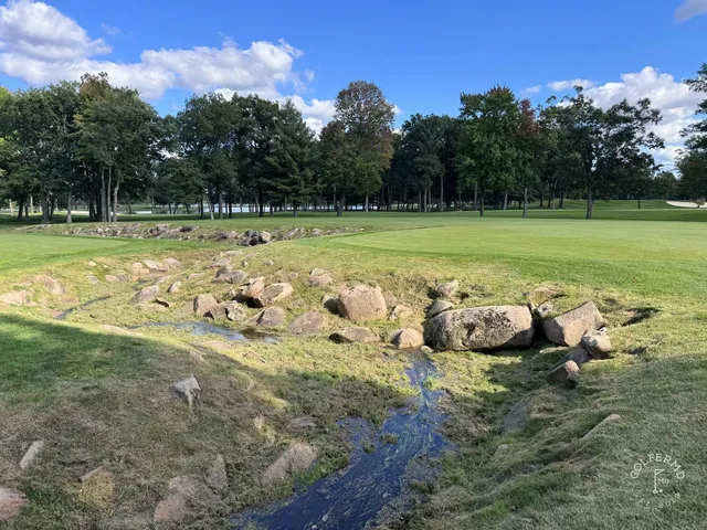 A golfer hitting a shot at SentryWorld, with the hole ahead.