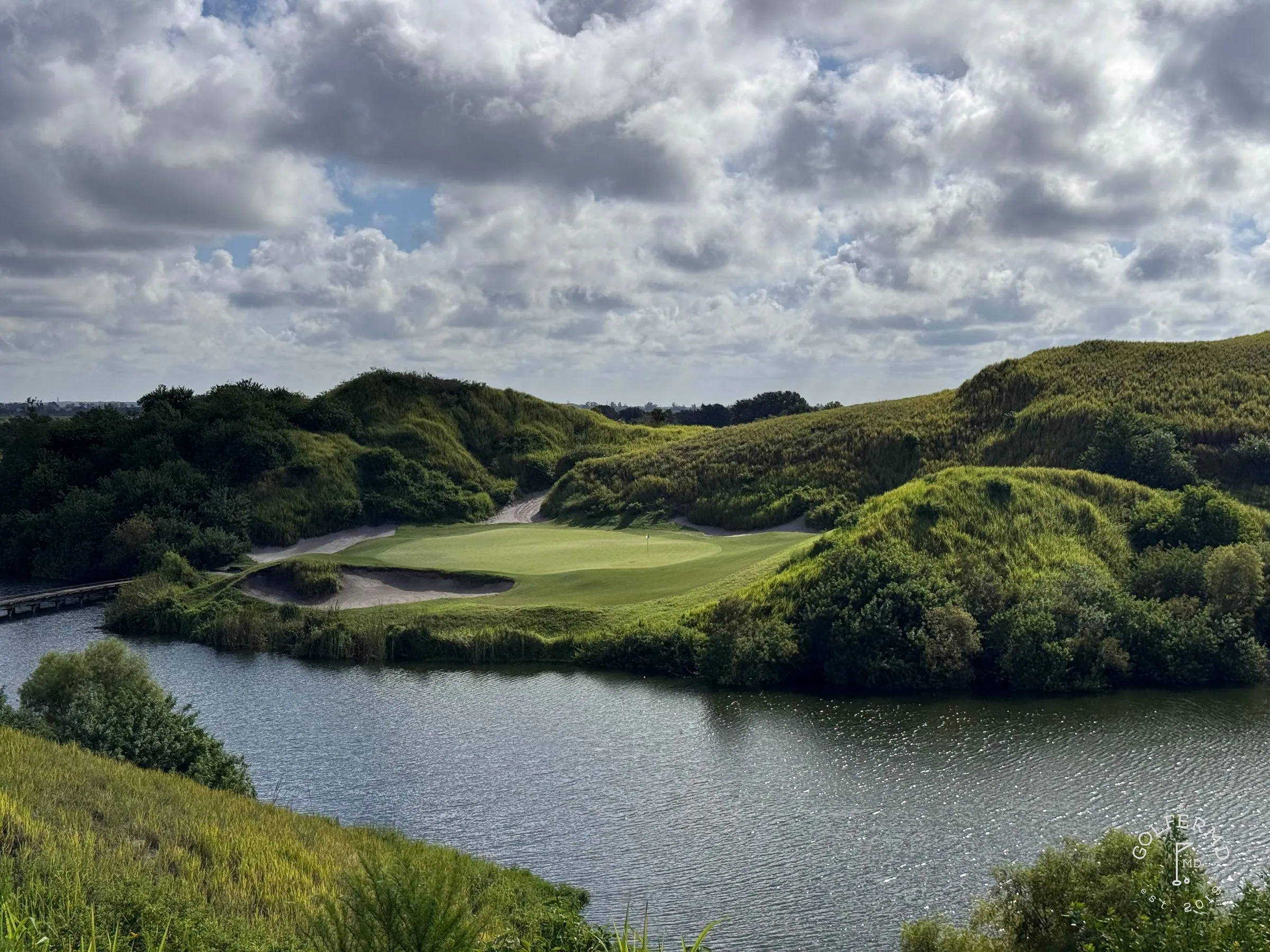 A wide sand bunker in the foreground, with the green and a pine-lined fairway beyond.