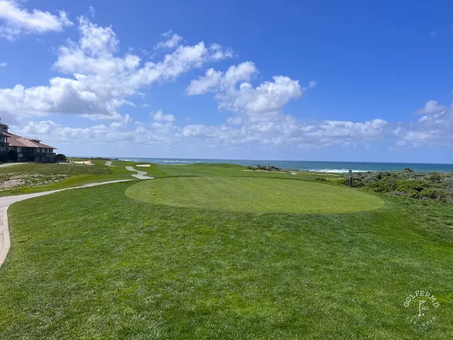 A green and flagstick beside the ocean at The Links at Spanish Bay, with dunes and a cypress tree.