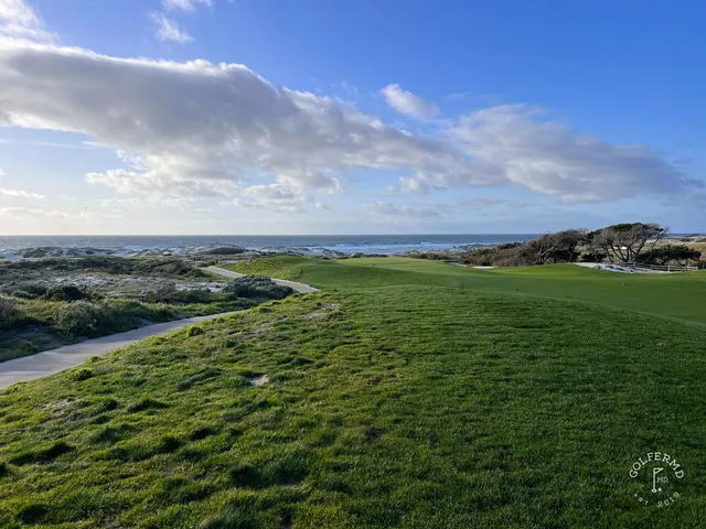 A golfer hitting a shot from the dunes at The Links at Spanish Bay, with the ocean behind the hole.