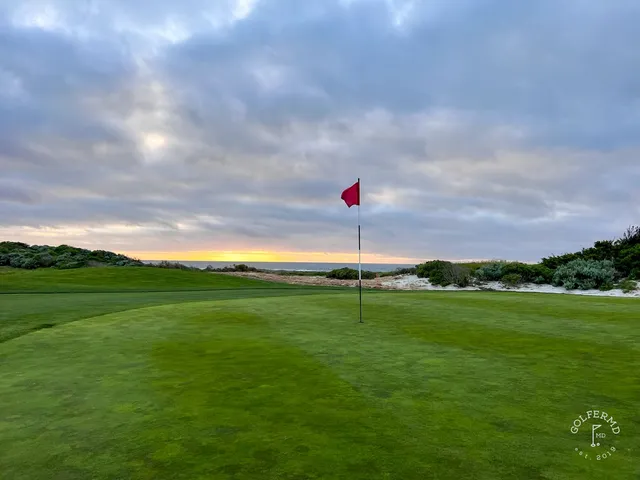 A green and flagstick beside the ocean at The Links at Spanish Bay, with dunes in the foreground.