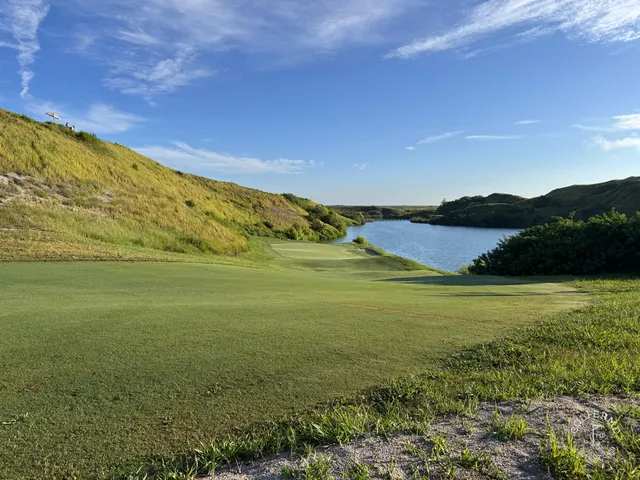 Sandy waste ground and long grass at Streamsong's Blue Course, with a distant green and the resort lodge on the horizon.