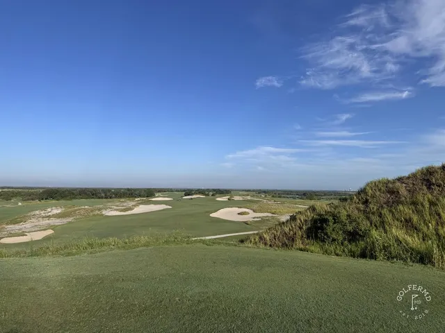 A green and flagstick at the Blue Course, seen across a sand bunker, with the Streamsong lodge in the distance.