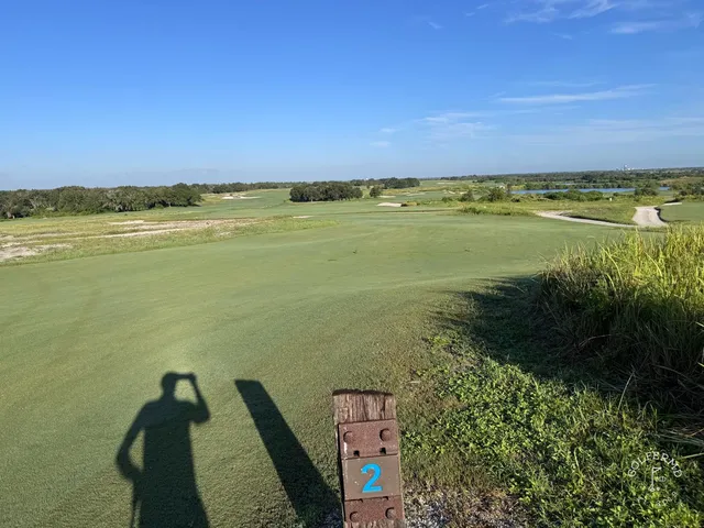 A green and flagstick at the Blue Course, with a sand bunker in the foreground and the Streamsong lodge behind the hole.