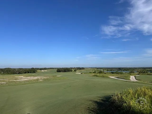 A golfer standing on a tee at the Blue Course, with a fairway, sand, and the Streamsong lodge ahead.
