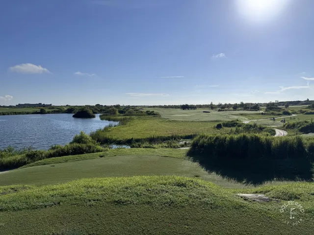 A fairway at the Blue Course running between sand and long grass toward a green and the Streamsong lodge.