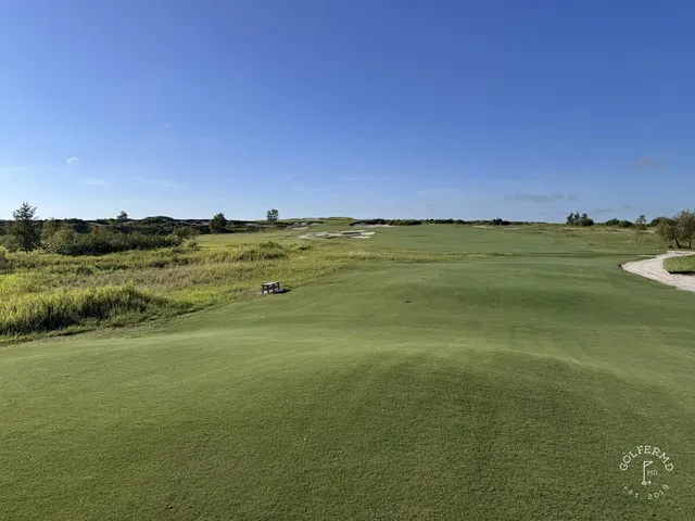 A green and flagstick at the Blue Course, with a large sand bunker in front and the Streamsong lodge behind the hole.