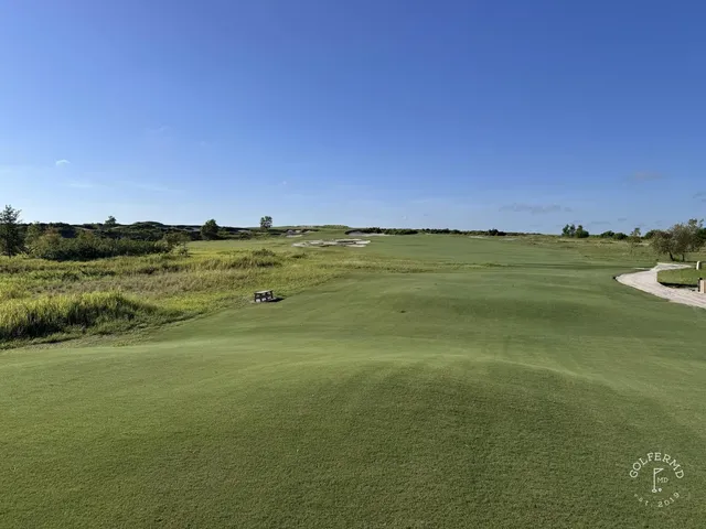 A wide view of the Blue Course, with a green, sand waste areas, and the Streamsong lodge on the horizon.
