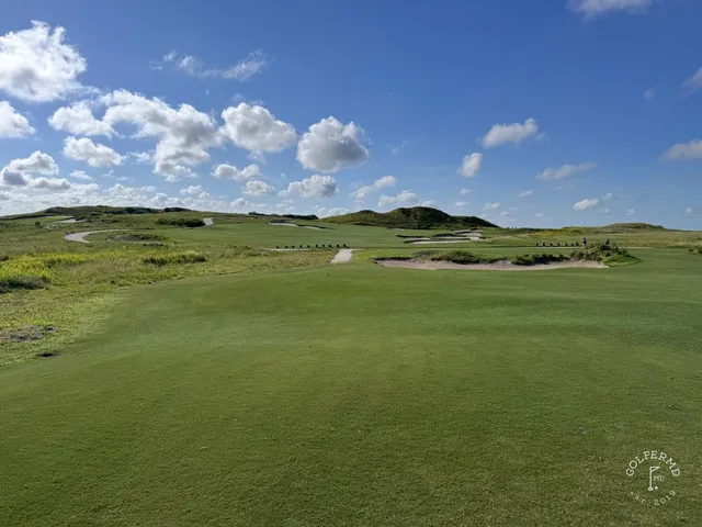 A golfer putting on a green at the Blue Course, with a sand bunker and the Streamsong lodge behind the hole.