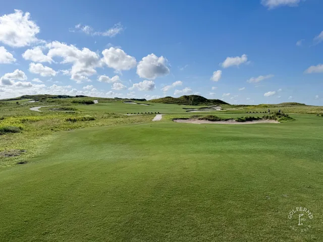 A golfer putting on a green at the Blue Course, with sand and the Streamsong lodge in the distance.