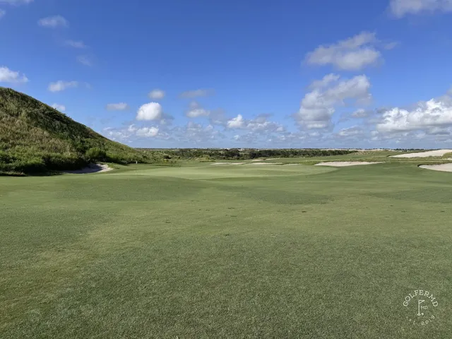 A fairway at the Blue Course curving through sand and long grass toward a distant green.
