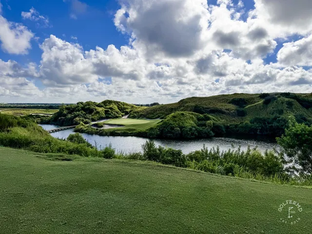 A green and flagstick at the Blue Course, with a sand bunker in front and rolling dunes behind the hole.