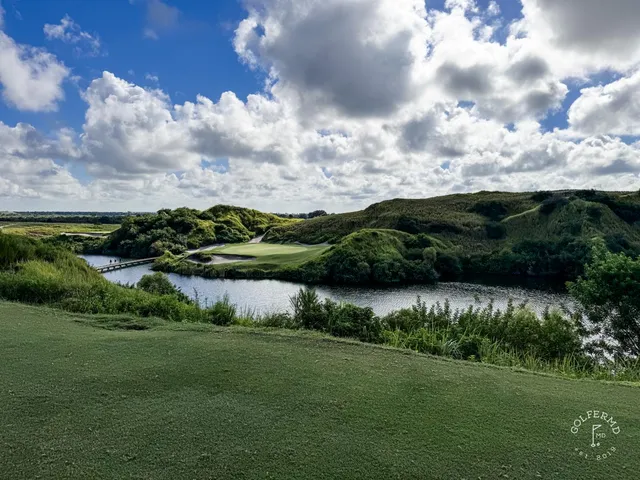 A green and flagstick at the Blue Course, seen from a sandy rise, with dunes and long grass around the hole.