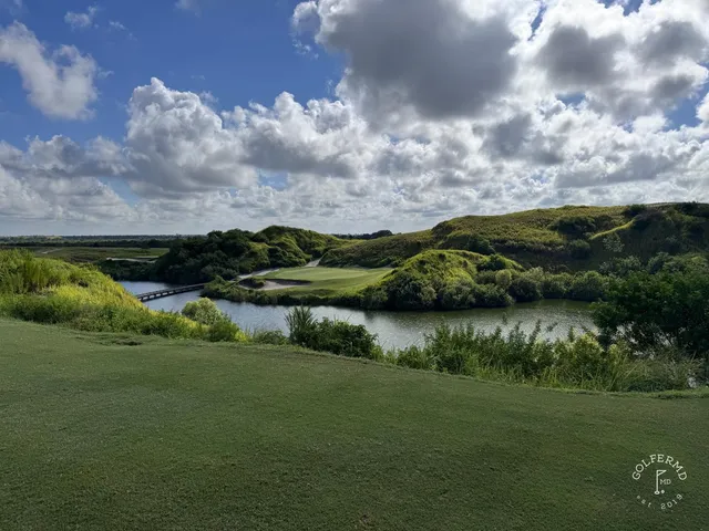 A wide sandy fairway at the Blue Course, with long grass and a distant green under a cloudy sky.