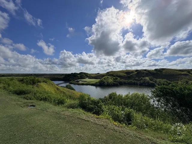 A golfer hitting a shot from a sandy waste area at the Blue Course, with a green and flagstick ahead.